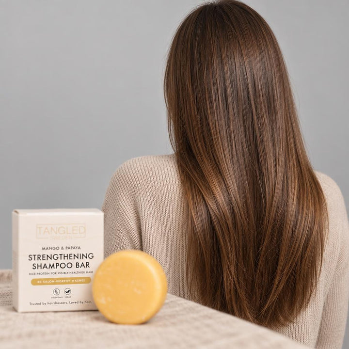 Kvinde med langt, skinnende brunt hår set bagfra og Tangled shampoobar med æske